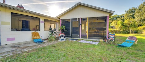 A house with a covered porch, a sliding glass door, and a small garden area with a lawn and two lawn chairs.