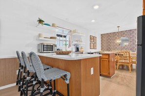 Una cocina moderna con una isla central, taburetes de bar y un área de comedor con un papel tapiz estampado.