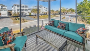 A sunlit room with a large window overlooking a residential area, a teal sofa with floral cushions, and a wooden table. - Steps to Sand! Home w/ 3 Decks in Sunset Beach (Sunset Beach)