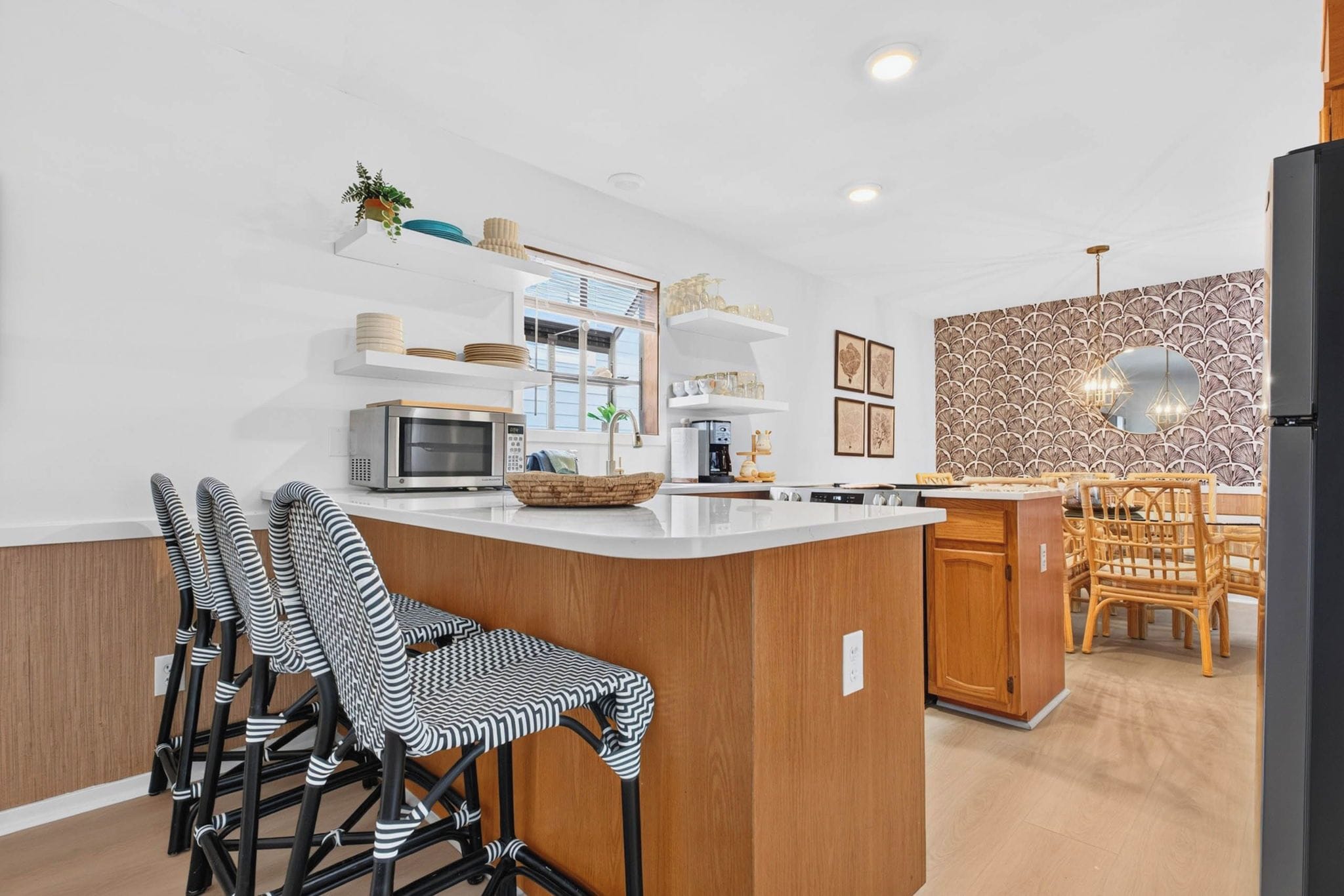 A modern kitchen with a central island, bar stools, and a dining area with a patterned wall.
