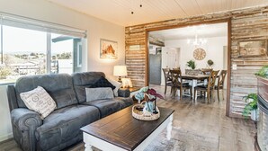 A living room with a dark leather sofa, a wooden coffee table, and a dining area with wooden chairs and a chandelier. - 2 Mi to Clear Lake: Pet-friendly Lakeport Retreat! (Lakeport)