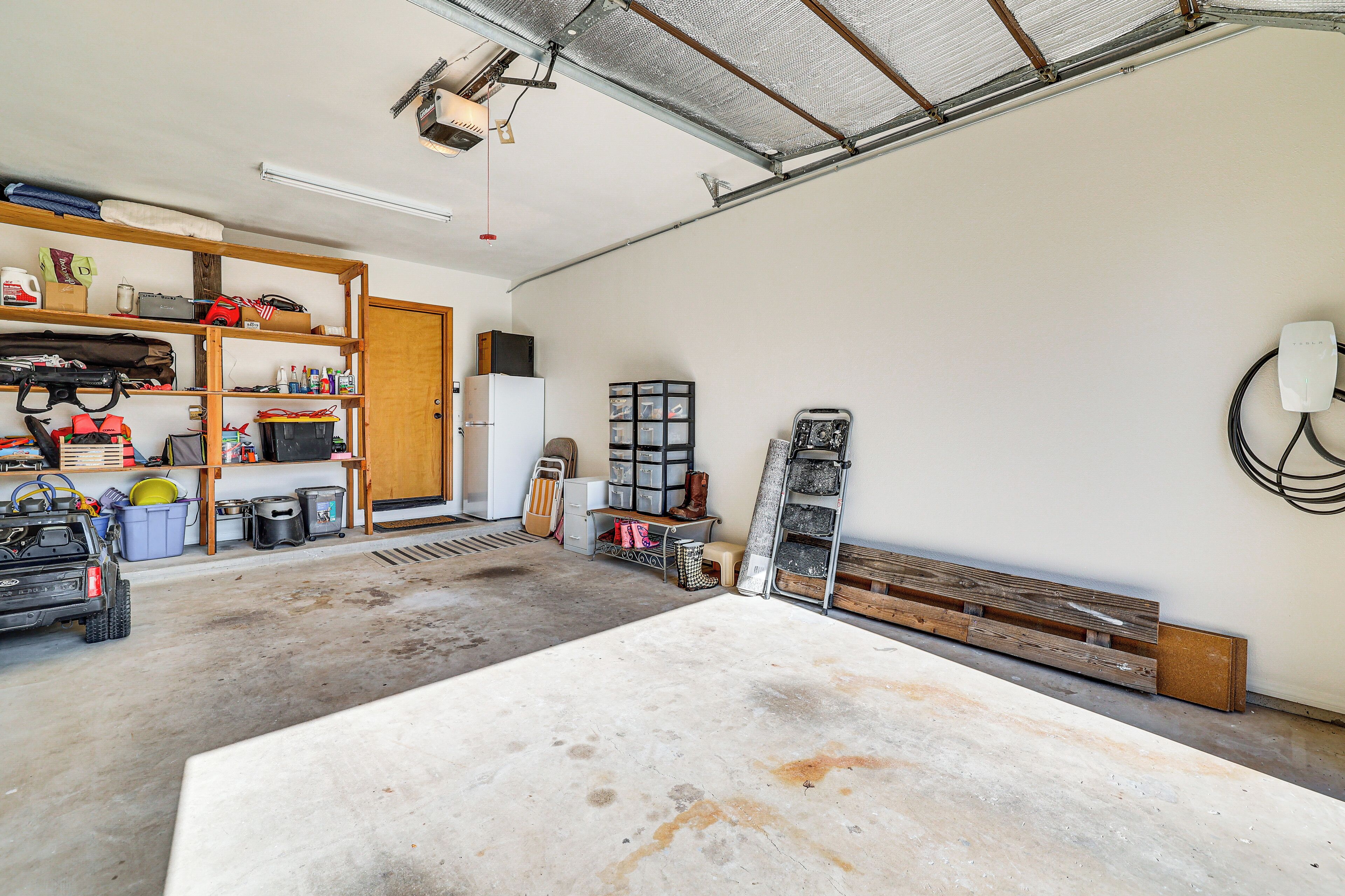 A garage with a workbench, shelves with tools and supplies, and a ladder.
