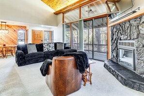 Ein modernes Wohnzimmer mit einem Ecksofa, einem Ledersitzhocker und einem Kamin aus Naturstein.