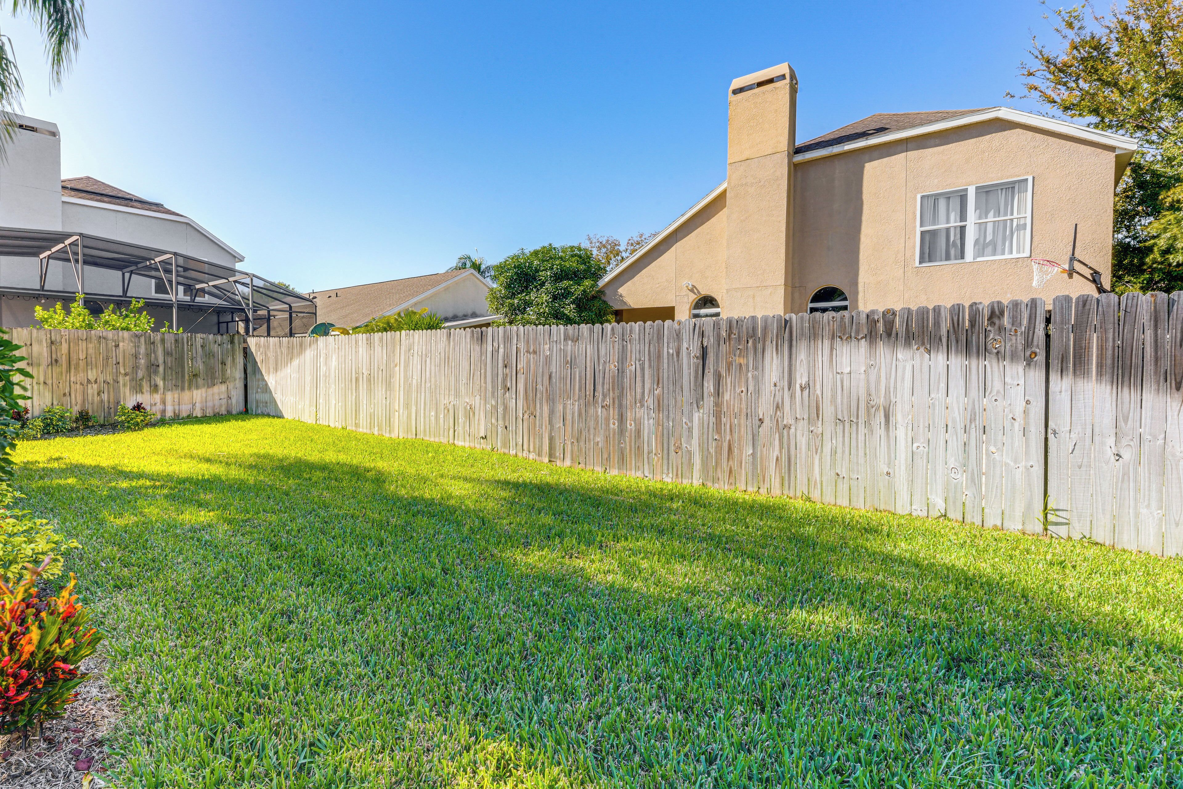 A residential backyard with a wooden fence, a grassy lawn, and a house with a chimney.