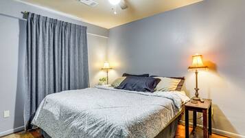 A bedroom with a bed, two bedside lamps, a ceiling fan, and a window with curtains.