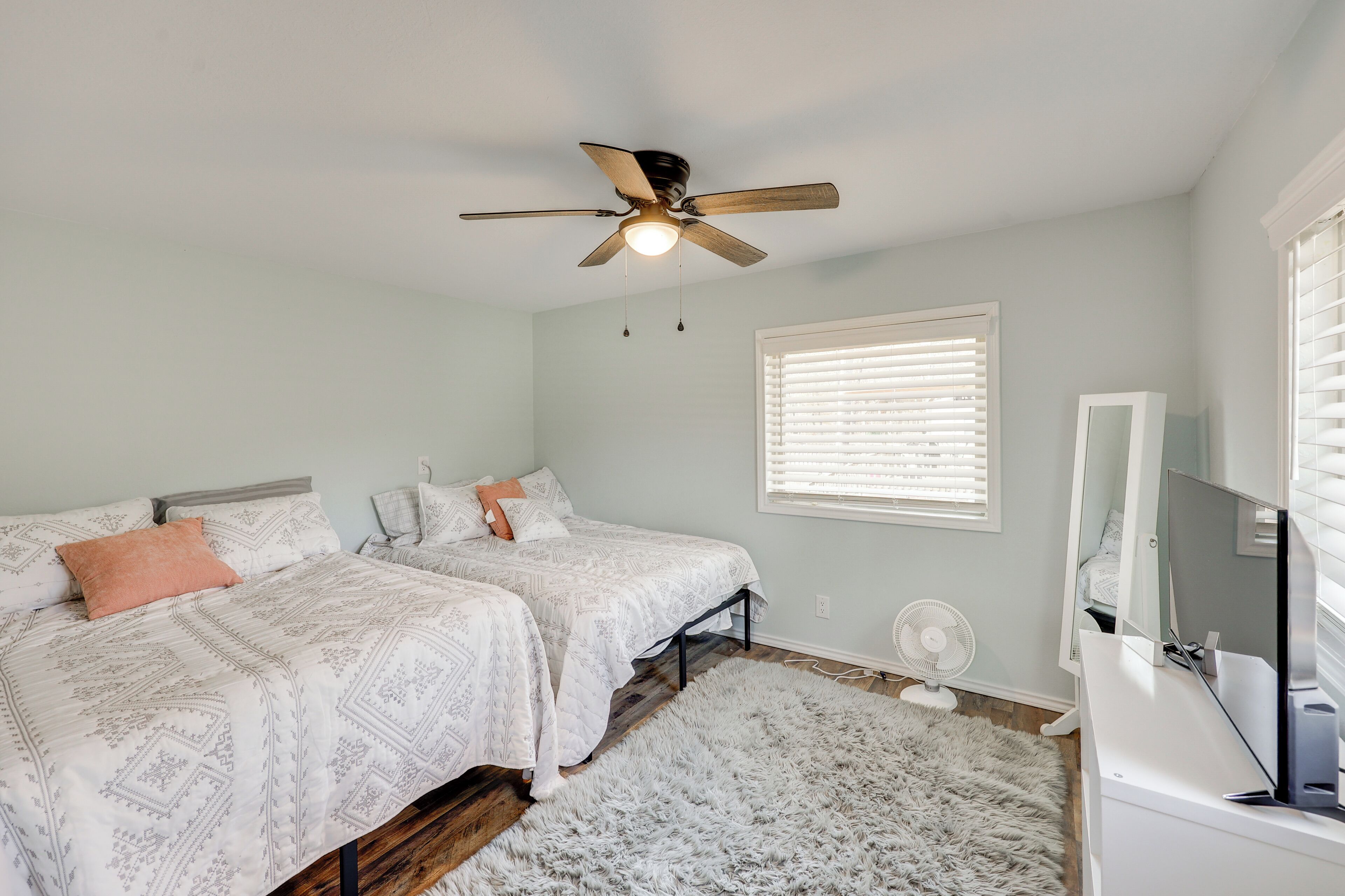 A bedroom with two beds, a ceiling fan, a TV, and a window with blinds.