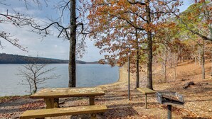 A picnic table and bench by a lake with trees and a bench in the background. - Bring Your Boat: Family Home Steps to Lake Greeson (Kirby)