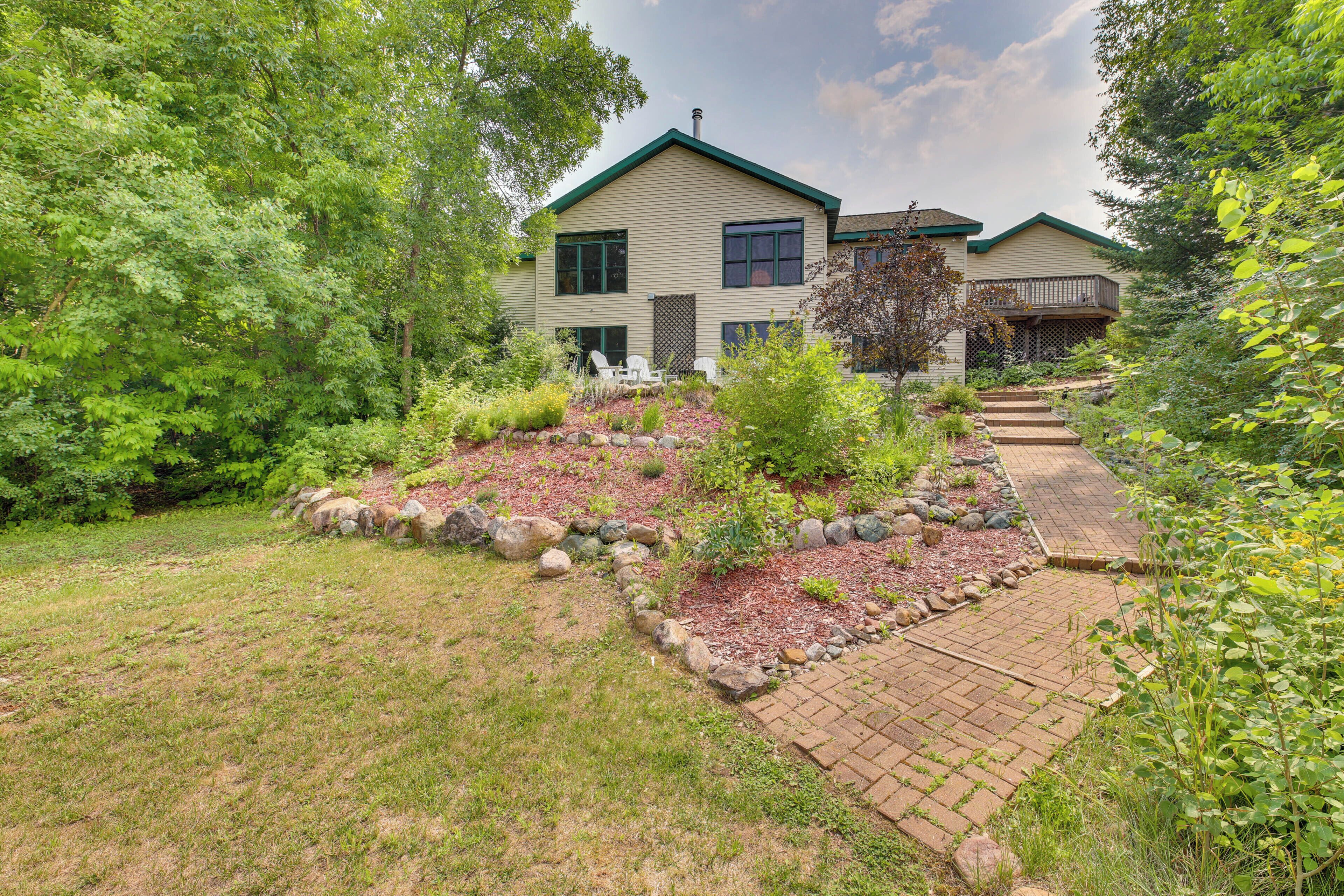 A two-story house with a landscaped garden, a paved pathway, and a visible chimney.