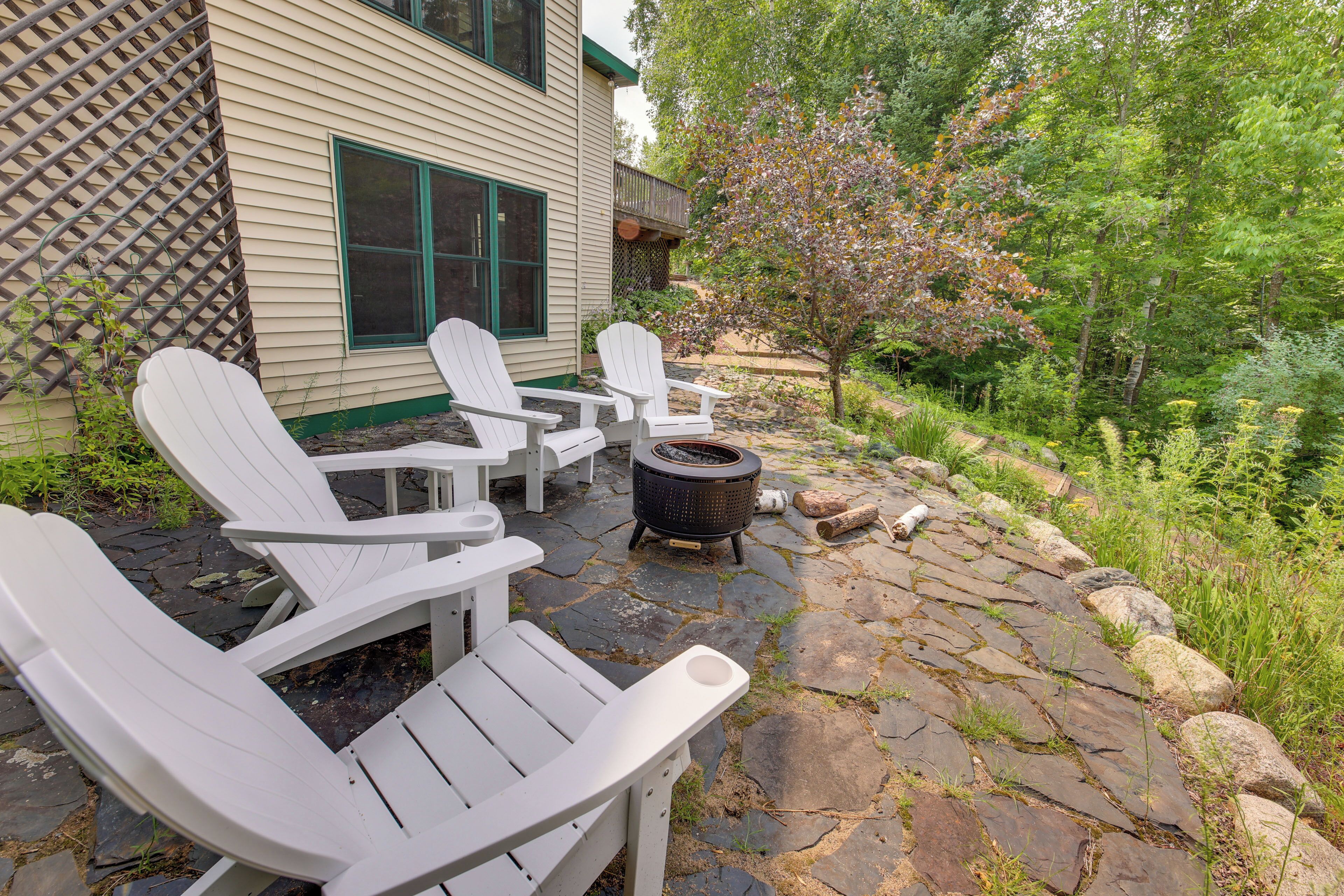 A patio with Adirondack chairs, a fire pit, and a stone pathway leading to a house with a lattice fence.