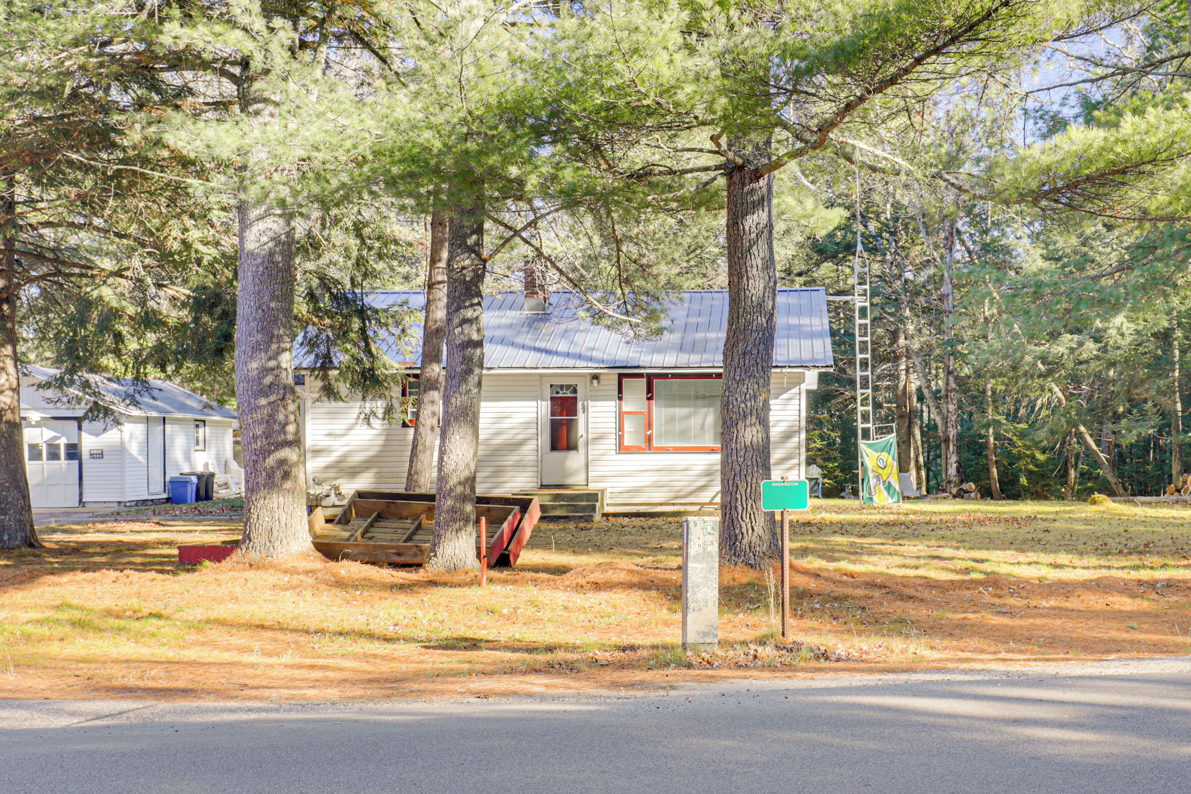 A small, single-story cabin with a metal roof, surrounded by trees.