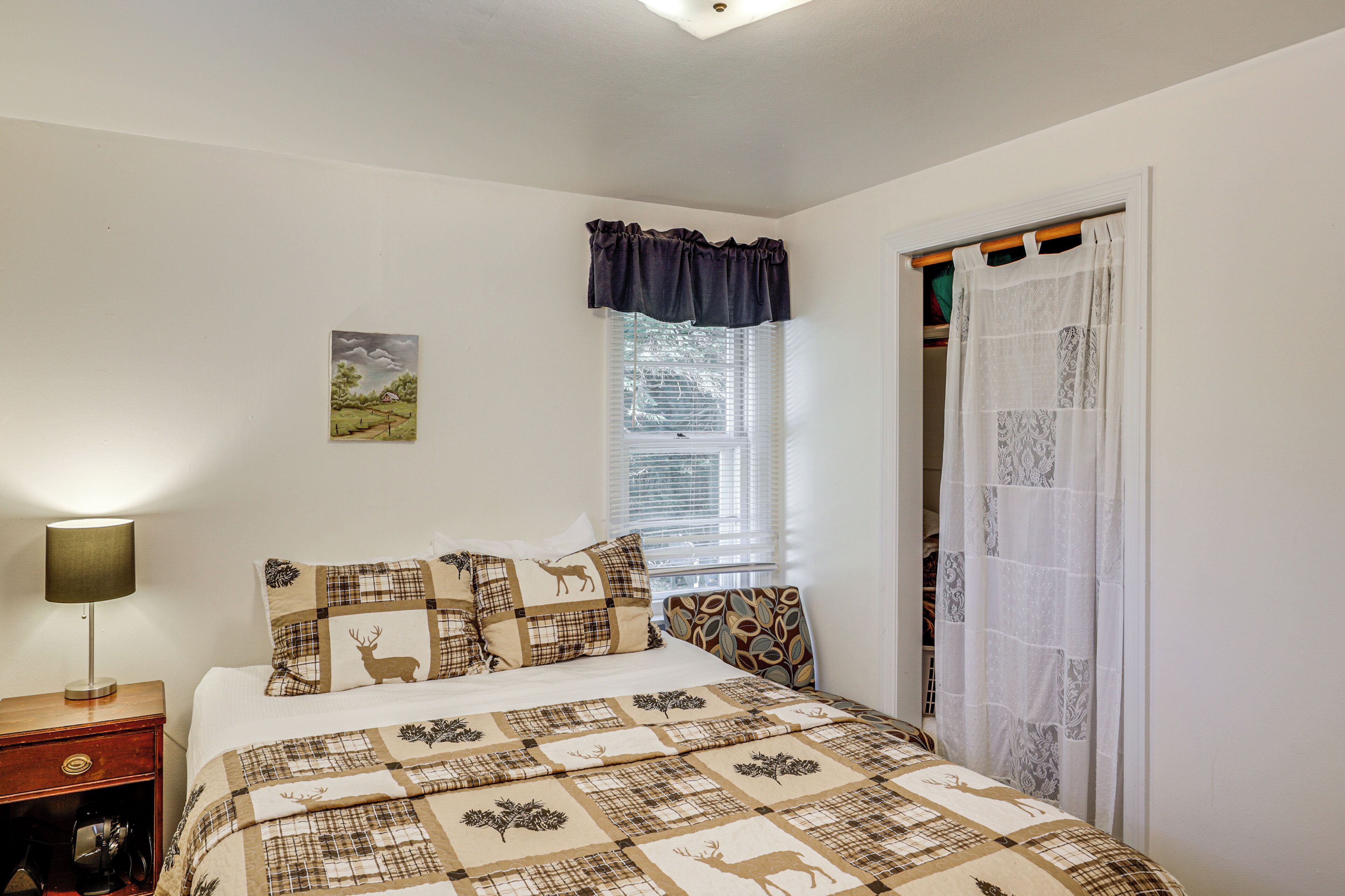 Une chambre à coucher comprenant un lit, une table de chevet, une lampe, une fenêtre avec des stores et une porte avec un rideau.