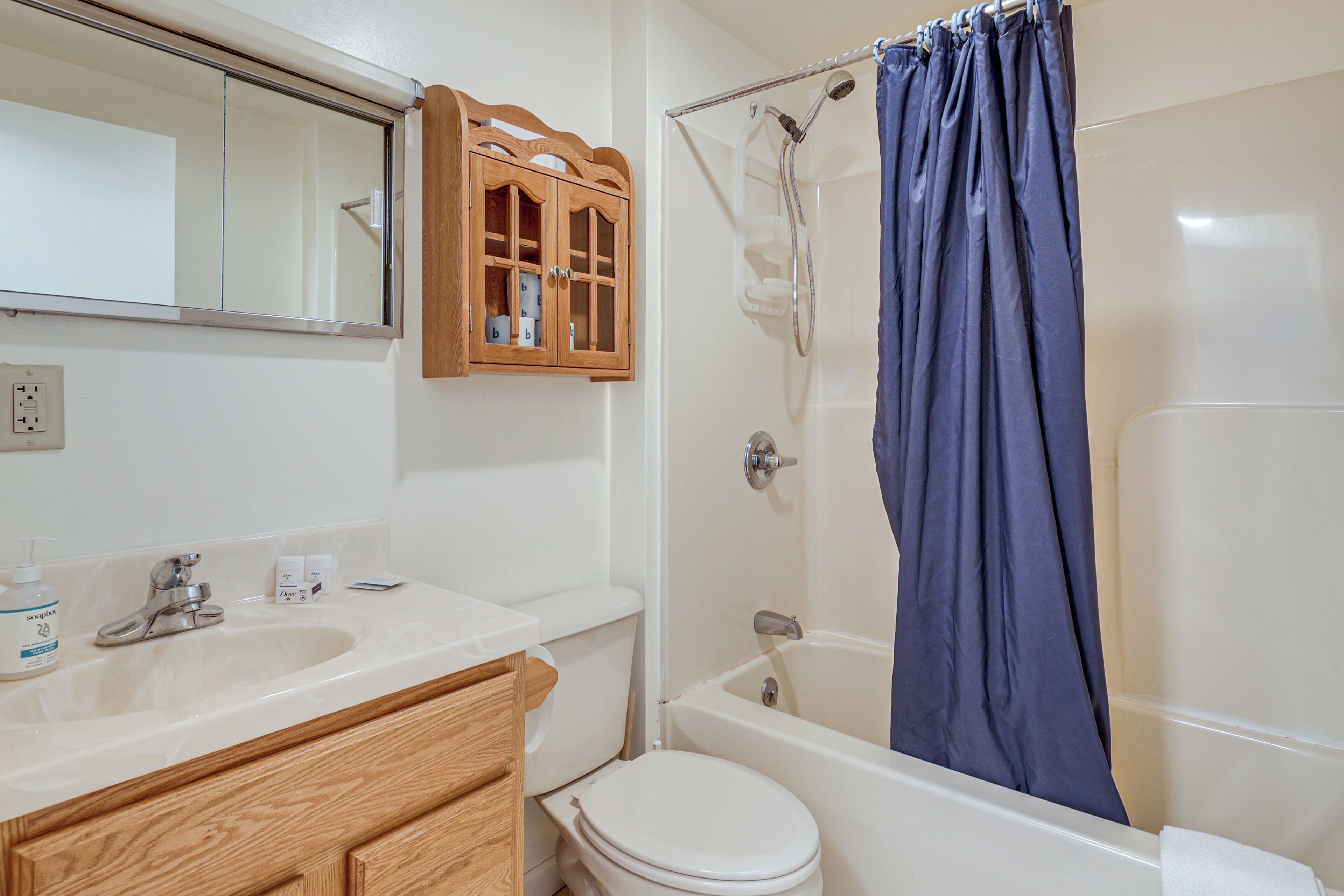 A bathroom with a white sink, wooden cabinets, a toilet, and a bathtub with a blue shower curtain.