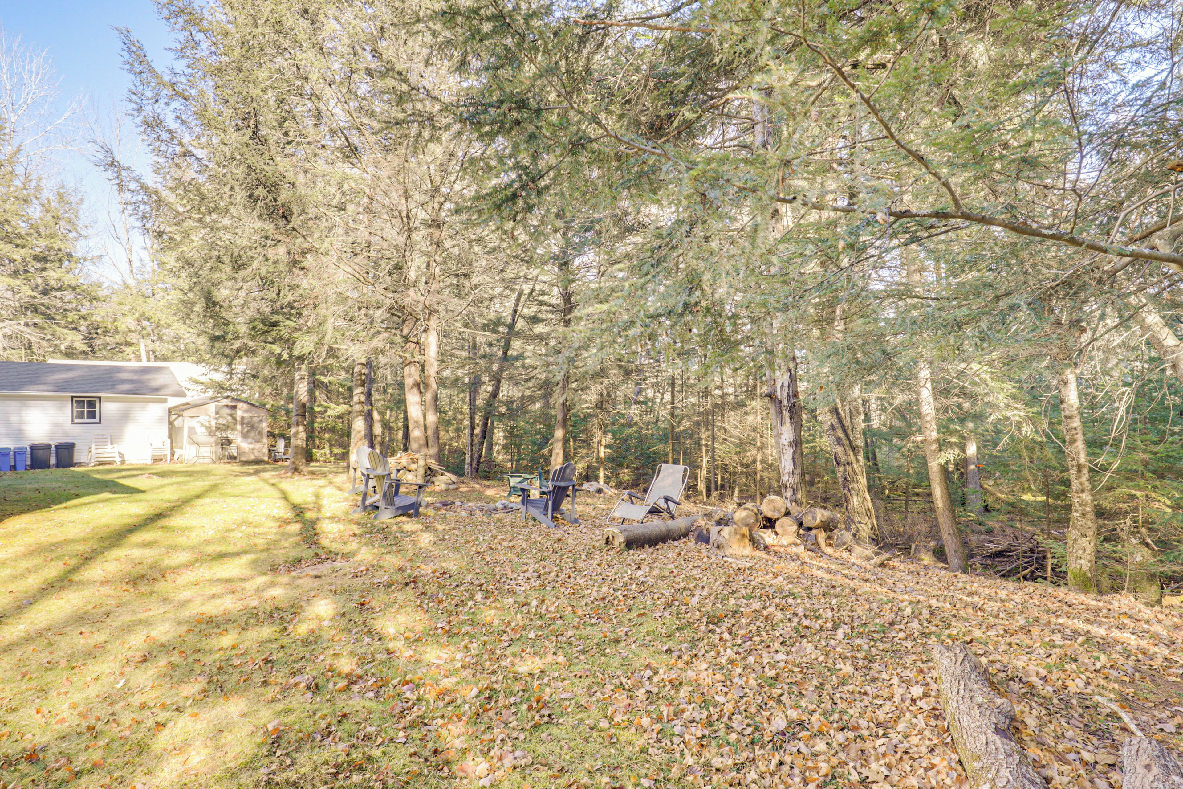 A forested area with a house, outdoor seating, and a log pile.