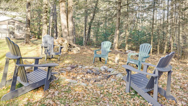 A forested area with several Adirondack chairs arranged around a small fire pit. - Year-round Chain of Lakes Retreat! Northwoods Home (Eagle River)