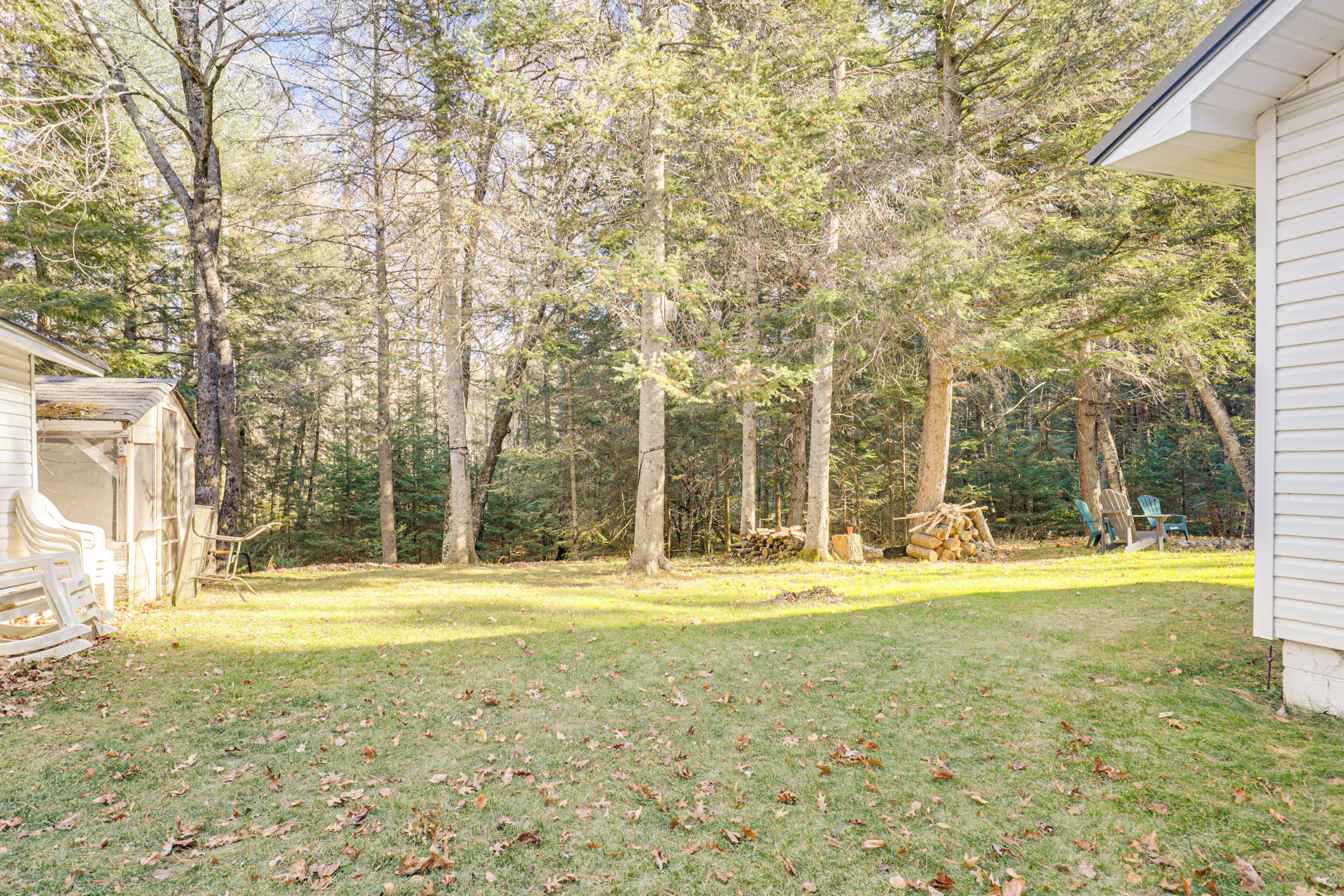 A backyard with a wooden deck, a pile of firewood, and a small shed.
