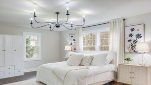 Une chambre à coucher avec un grand lit, un lustre, une table de chevet, une armoire et une fenêtre avec des rideaux.