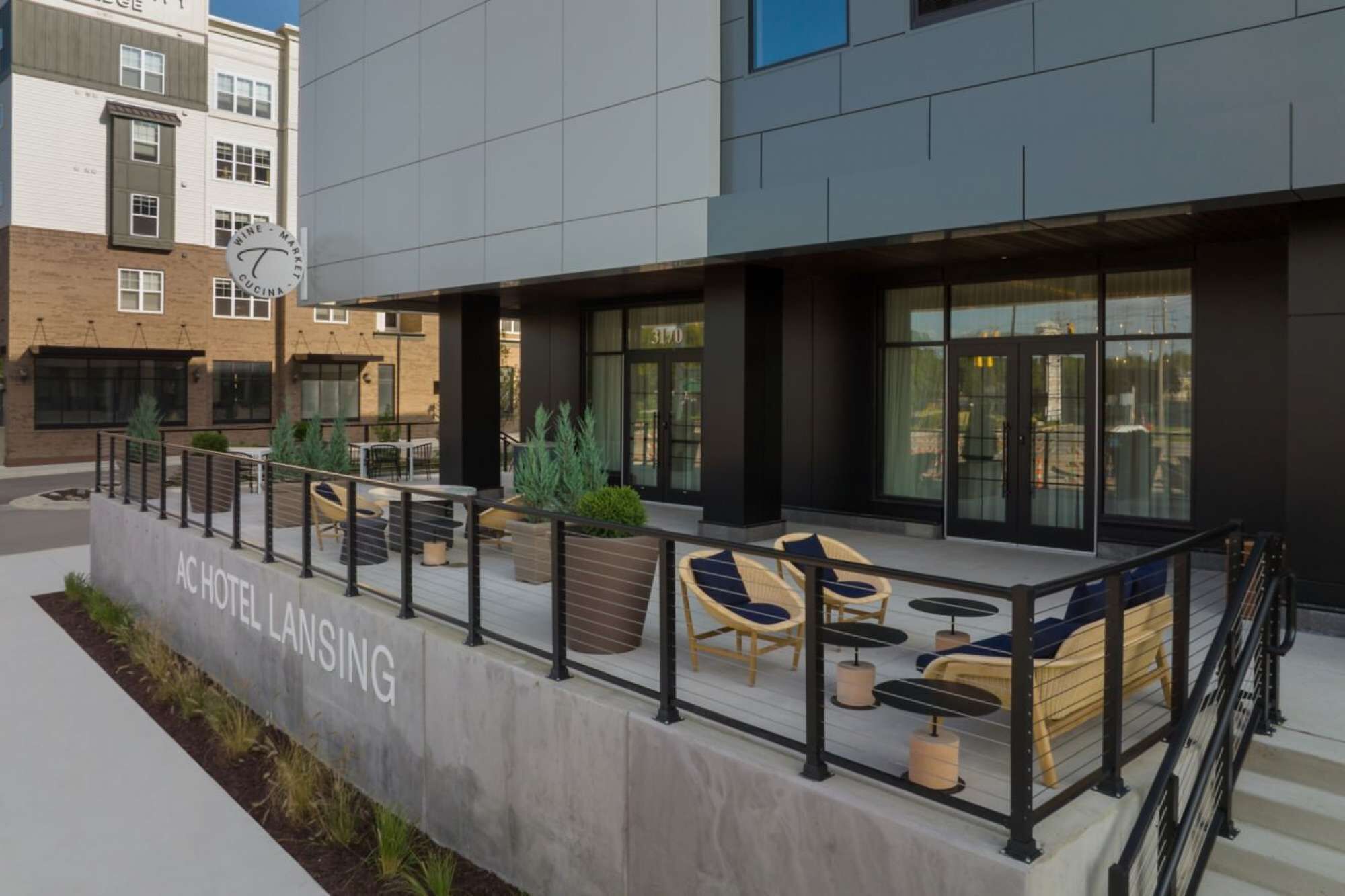 A hotel with outdoor seating, a concrete barrier, and a sign reading "AC HOTEL LANSING".