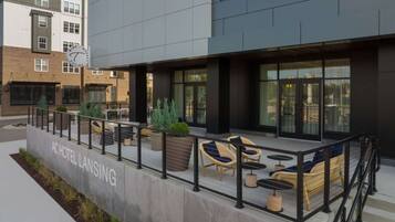 A hotel with outdoor seating, a concrete barrier, and a sign reading "AC HOTEL LANSING".