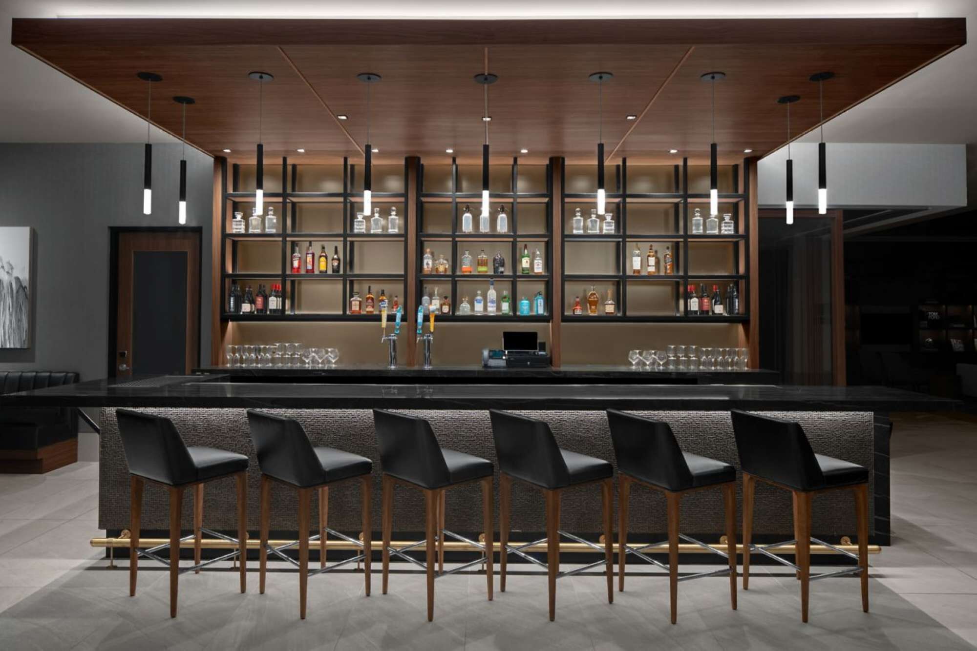 A bar area with a long counter, multiple shelves of bottles, and six bar stools.
