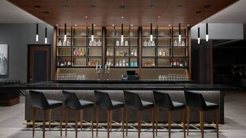 A bar area with a long counter, multiple shelves of bottles, and six bar stools.