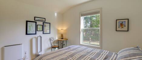 Un dormitorio con cama, radiador, silla, mesa y ventana.