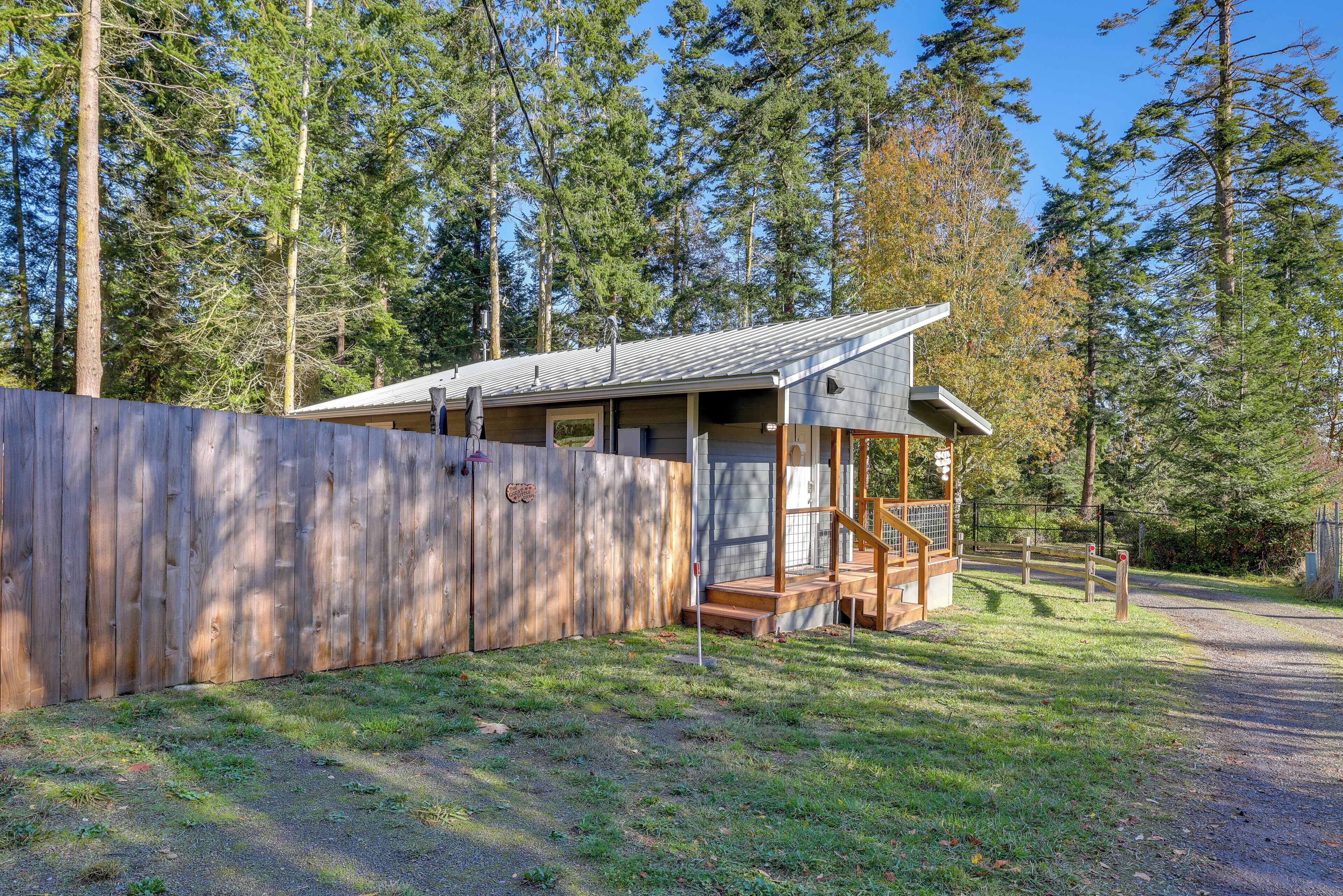 A cabin with a wooden deck, a covered porch, and a fenced yard surrounded by tall trees.