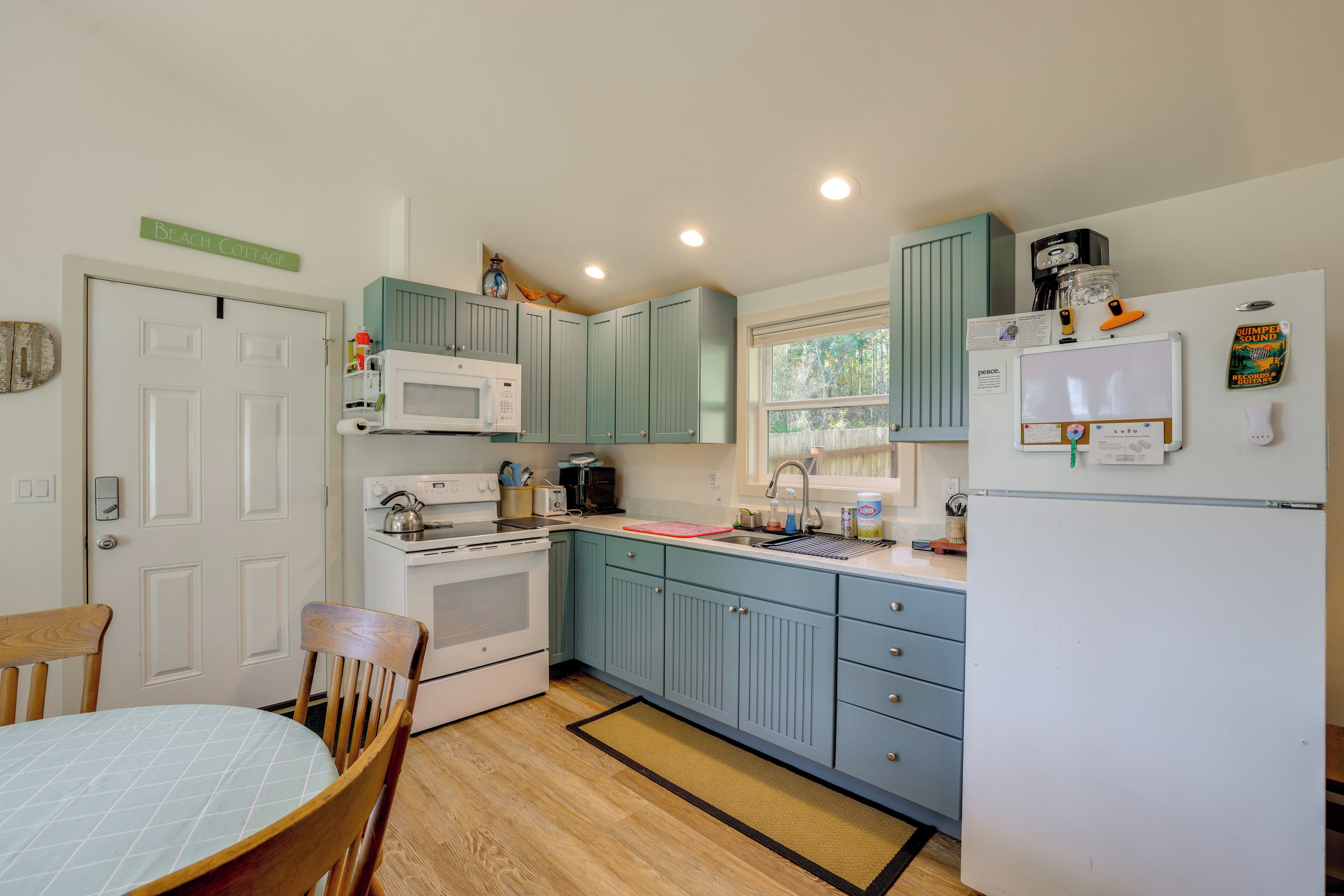 A kitchen with teal cabinets, a white refrigerator, a microwave, a stove, and a dining table with chairs.