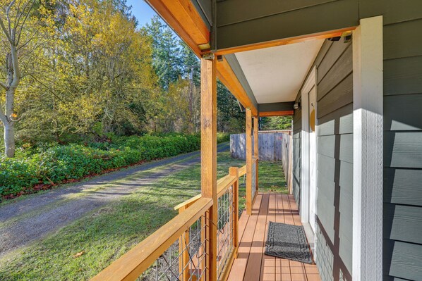 A covered porch with a wooden railing, a gravel path, and a view of a wooded area. - Hike & Relax Fireside: Nordland Gem w/ Deck & Yard (Nordland)