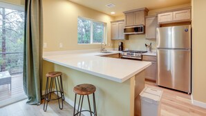 A modern kitchen with a large island, bar stools, stainless steel appliances, and a view of the outdoors. - Cozy Woodland Retreat in the Pines, Near Prescott! (Prescott)