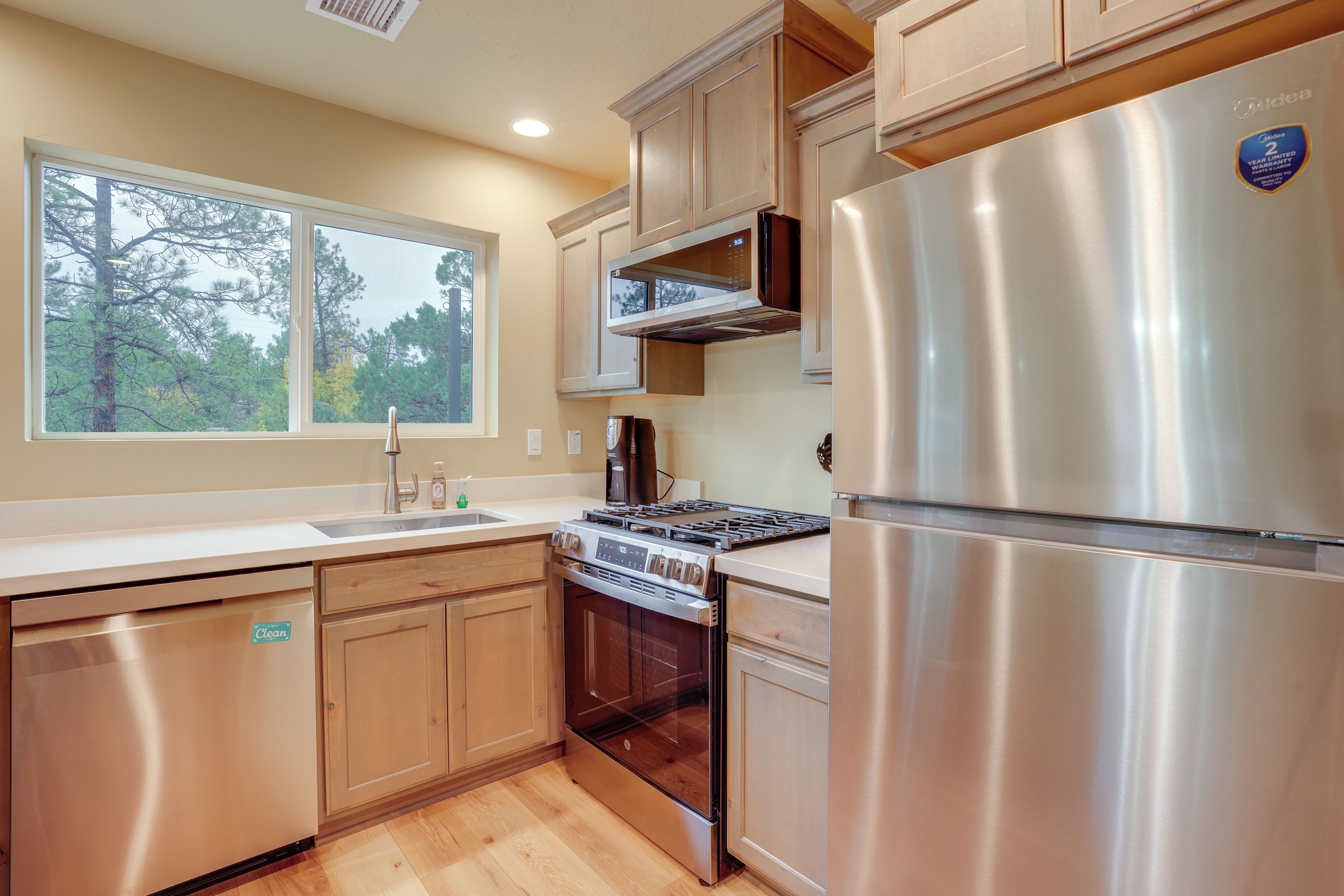 Una cucina moderna con elettrodomestici in acciaio inossidabile, mobili in legno e un'ampia finestra con vista sugli alberi.