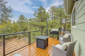Eine Holzterrasse mit Gartenmöbeln, einem Grill und Blick auf Bäume.