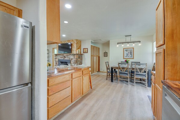 A kitchen with wooden cabinets, a stainless steel refrigerator, a stone backsplash, and a dining area with a wooden table and chairs. - Dog Friendly! Peaceful Wooded Retreat in Prescott (Prescott)