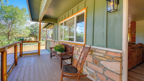 A wooden deck with a rocking chair and a potted plant, a stone wall, and a wooden bench. - Dog Friendly! Peaceful Wooded Retreat in Prescott (Prescott)