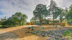A two-story house with a stone facade, large windows, and a front yard with a rock garden and trees. - Dog Friendly! Peaceful Wooded Retreat in Prescott (Prescott)