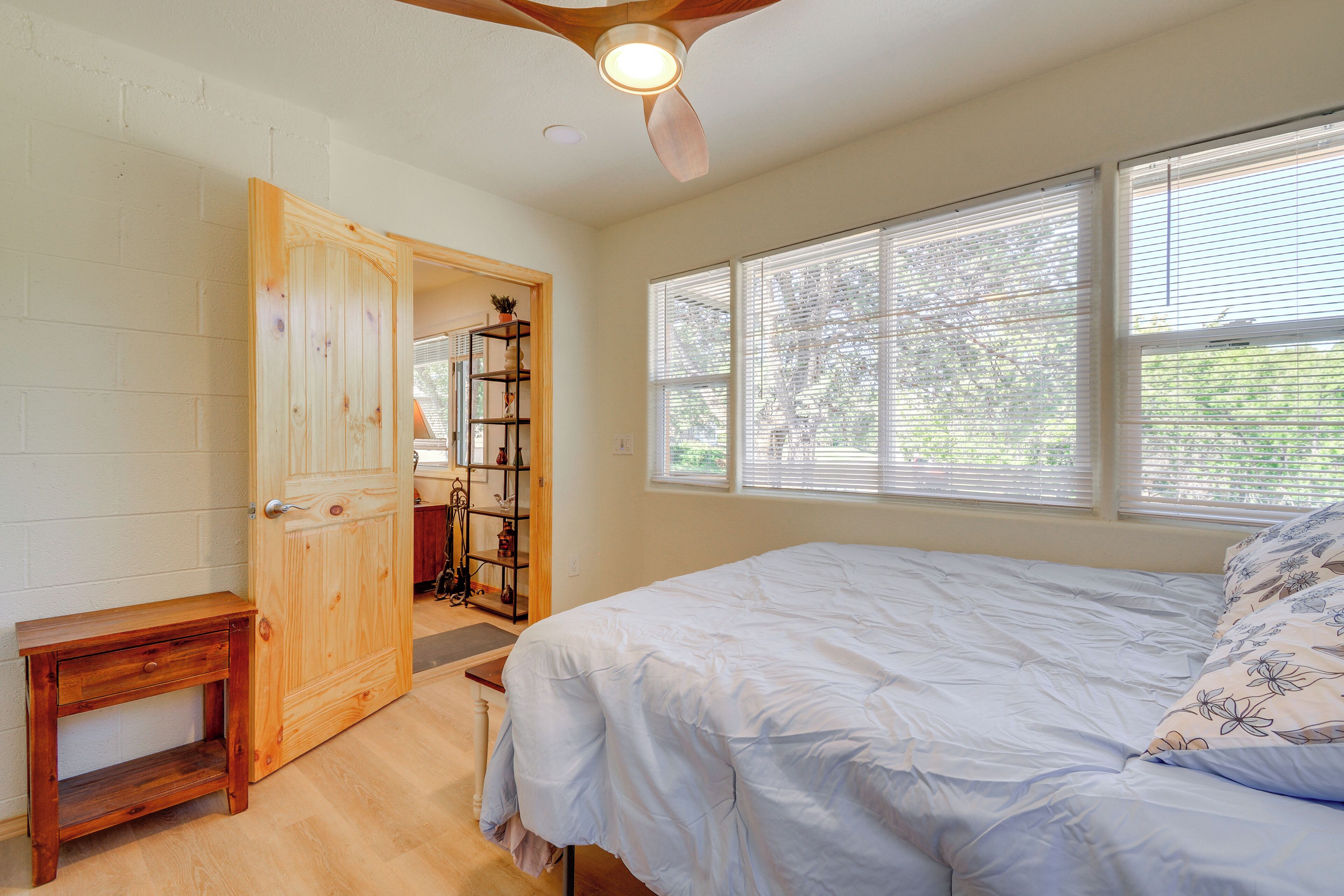 Un dormitorio con cama, una puerta de madera, una mesita y una ventana con persianas.