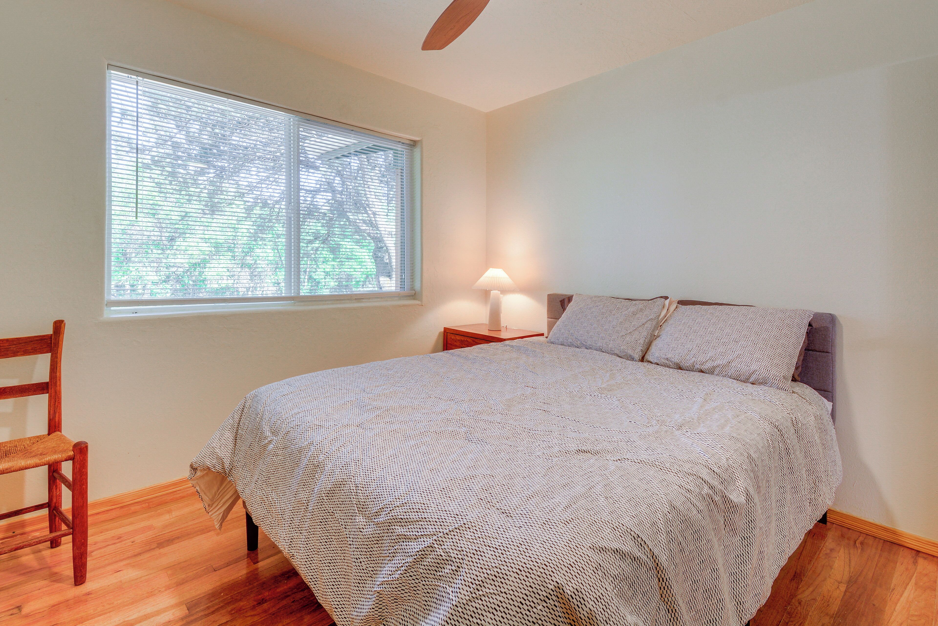 A bedroom with a bed, a window, a chair, and a nightstand with a lamp.