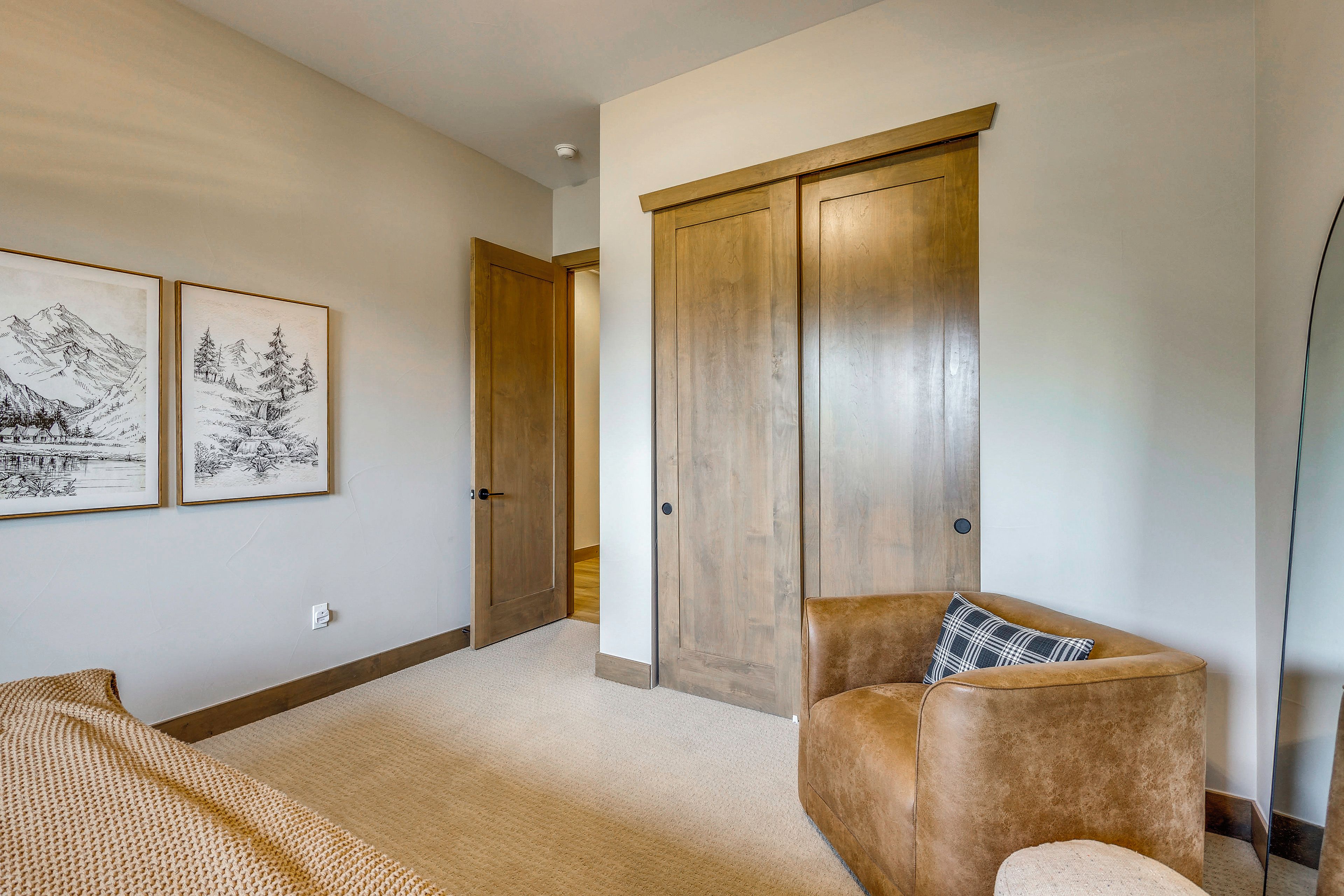 Una habitación con un sillón de cuero marrón, un armario de madera y dos cuadros de paisajes en la pared.