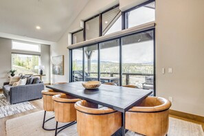 A modern dining area with a large table and leather chairs, large windows with a view of a mountainous landscape, and a cozy seating area with a sofa and a lamp. - Luxe Home w/ Hot Tub and Views in Winter Park! (Winter Park)