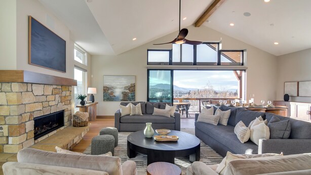 A spacious living room with a stone fireplace, a large gray sofa, and a dining area with a view of the mountains. - Luxe Home w/ Hot Tub and Views in Winter Park! (Winter Park)