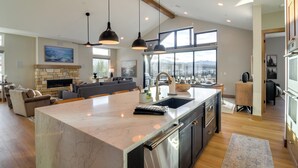 A spacious kitchen with a large island, modern pendant lights, and a stone fireplace. - Luxe Home w/ Hot Tub and Views in Winter Park! (Winter Park)