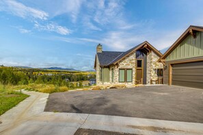A two-story stone house with a garage, a driveway, and a view of a forested valley. - Luxe Home w/ Hot Tub and Views in Winter Park! (Winter Park)