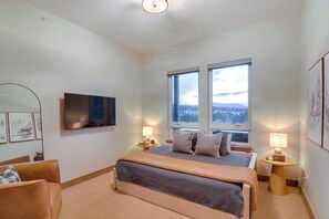 A modern bedroom with a large bed, two bedside tables with lamps, a flat-screen TV on the wall, and a window with a view of the mountains. - Luxe Home w/ Hot Tub and Views in Winter Park! (Winter Park)