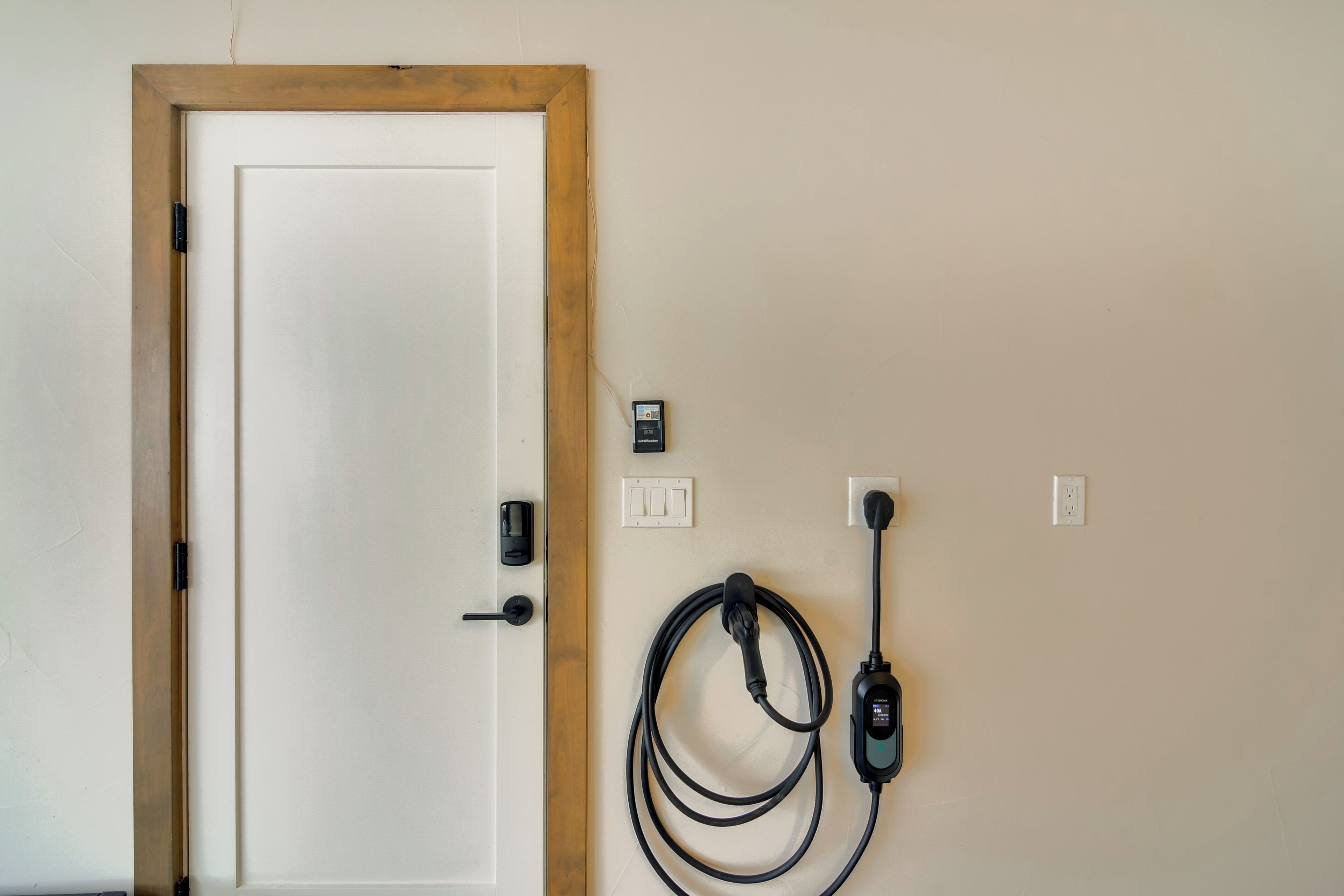 A door with a wooden frame, a wall-mounted electrical outlet, and a charging station with a cable.