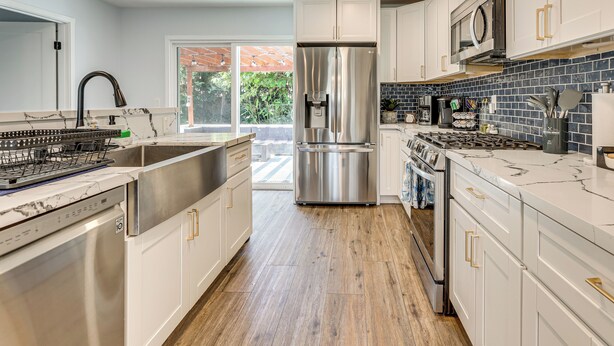Una cocina moderna con electrodomésticos de acero inoxidable, armarios blancos y piso de madera.