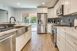 Une cuisine moderne dotée d’appareils électroménagers en acier inoxydable, de meubles blancs et d’un plancher en bois.