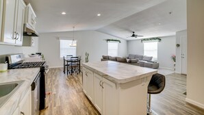 A modern kitchen with white cabinetry, a central island, and a dining area with a table and chairs. - Explore Temecula Wine Country! Mtn-view Home (Wildomar)