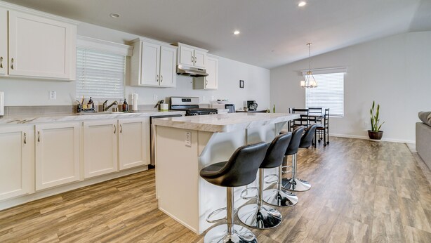 A modern kitchen with white cabinets, a central island with bar stools, a dining area with a table and chairs, and a potted plant. - Explore Temecula Wine Country! Mtn-view Home (Wildomar)