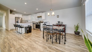 A modern kitchen with white cabinets, stainless steel appliances, and a dining area with a table and chairs. - Explore Temecula Wine Country! Mtn-view Home (Wildomar)