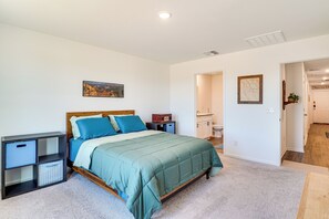 A bedroom with a bed, a nightstand, a shelf unit, and a door leading to a bathroom. - 6 Mi to State Park: Newly Built Home in Benson! (Benson)