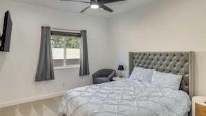 Una camera da letto con una testiera trapuntata, un letto con copriletto a motivi geometrici, una poltrona grigia, un comodino con una lampada e una finestra con tende grigie.